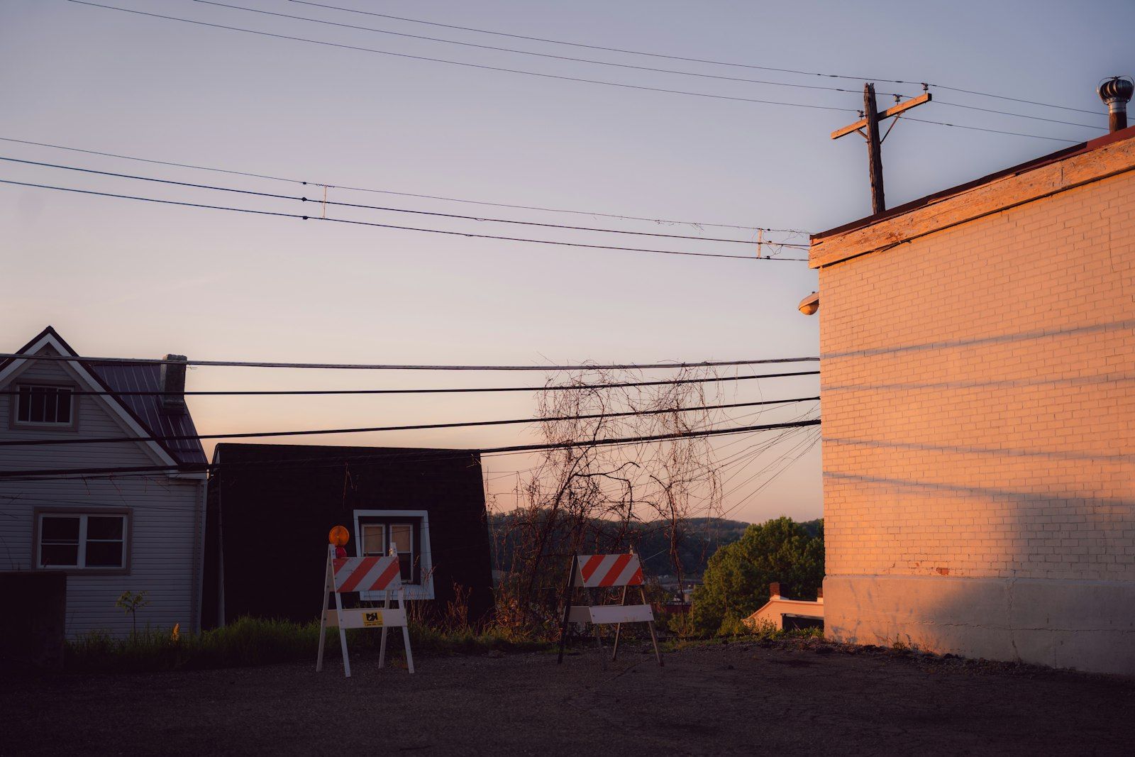 Warm sunset over buildings with power lines and striped barriers
